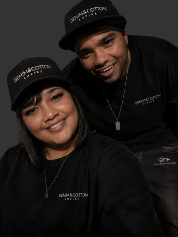 Two people wearing black 'Denim & Cotton Empire' hats and shirts against a dark background.